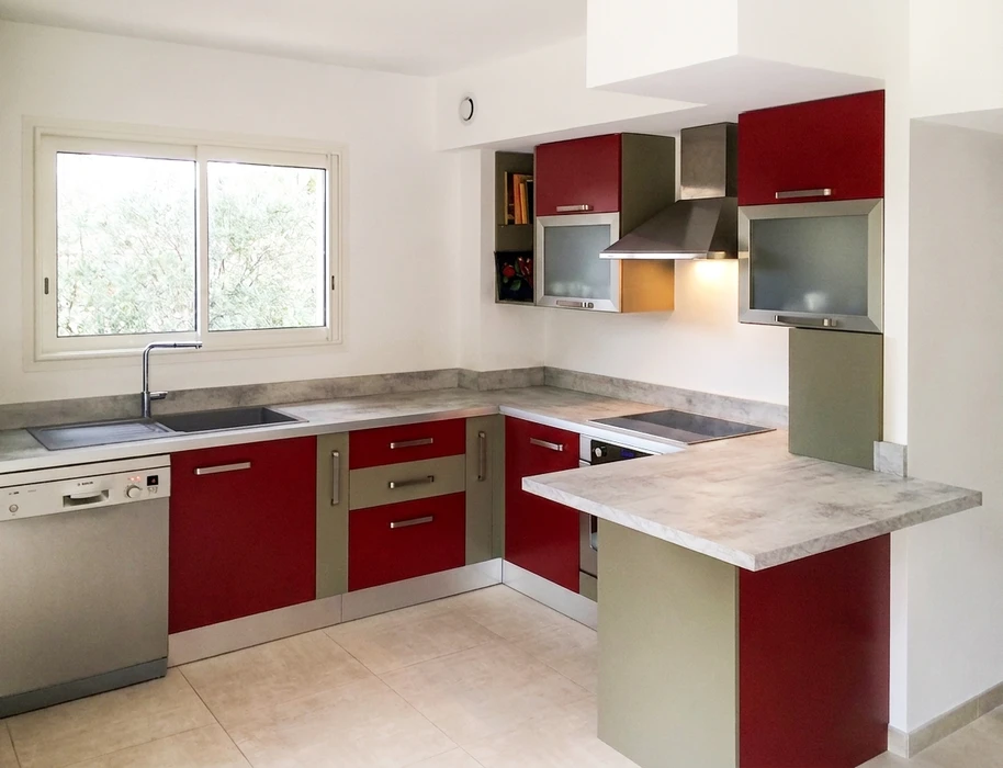 Photographie d'une cuisine ouverte moderne et haut de gamme, avec mobilier intégré en bois ou MDF laqué ou mélaminé, plan de travail épuré, appareils électroménagers haut de gamme intégrés, éclairage sophistiqué, aménagement spacieux montrant une réalisation complète de menuiserie sur mesure. La cuisine doit refléter un savoir-faire artisanal contemporain et un haut niveau de finition.