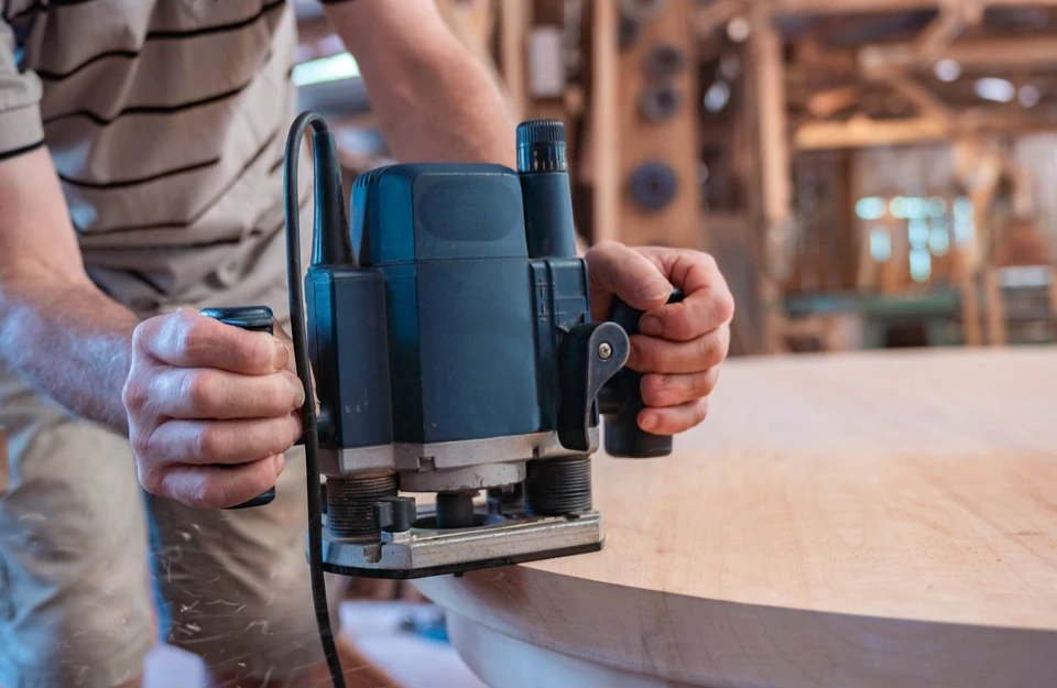 Atelier de menuiserie intérieur avec artisan utilisant une défonceuse électrique sur panneau de bois